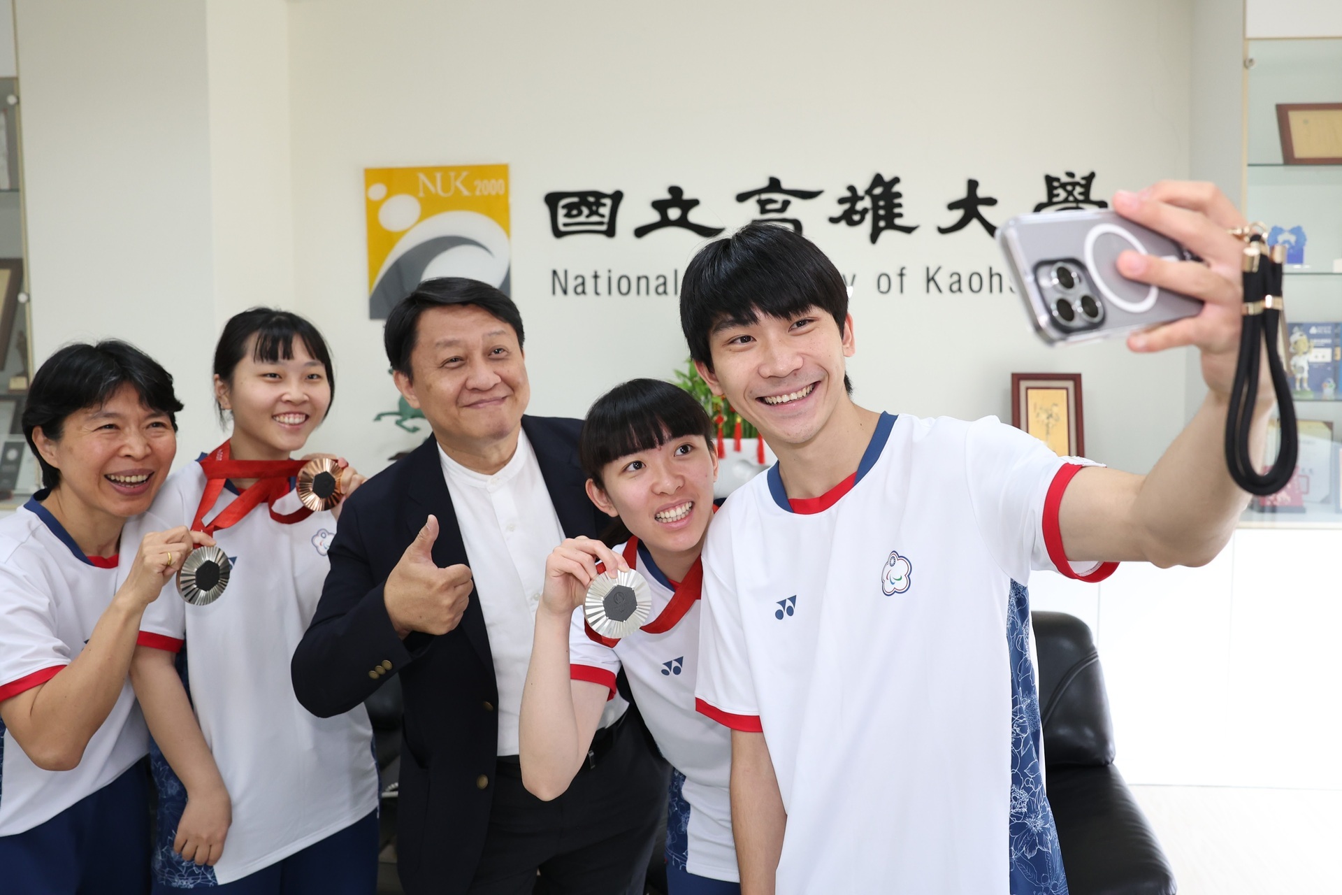 President Chi-Jen Chen of the National University of Kaohsiung (center) commends Ming-Yue Wang (first from left), Shiau-Wen Tian (second from left), Tzu-Yu Lin (second from right), and Jin-Sian Su for their outstanding performances in Paralympic table tennis. The mentor and students joyfully pose for a group photo.01