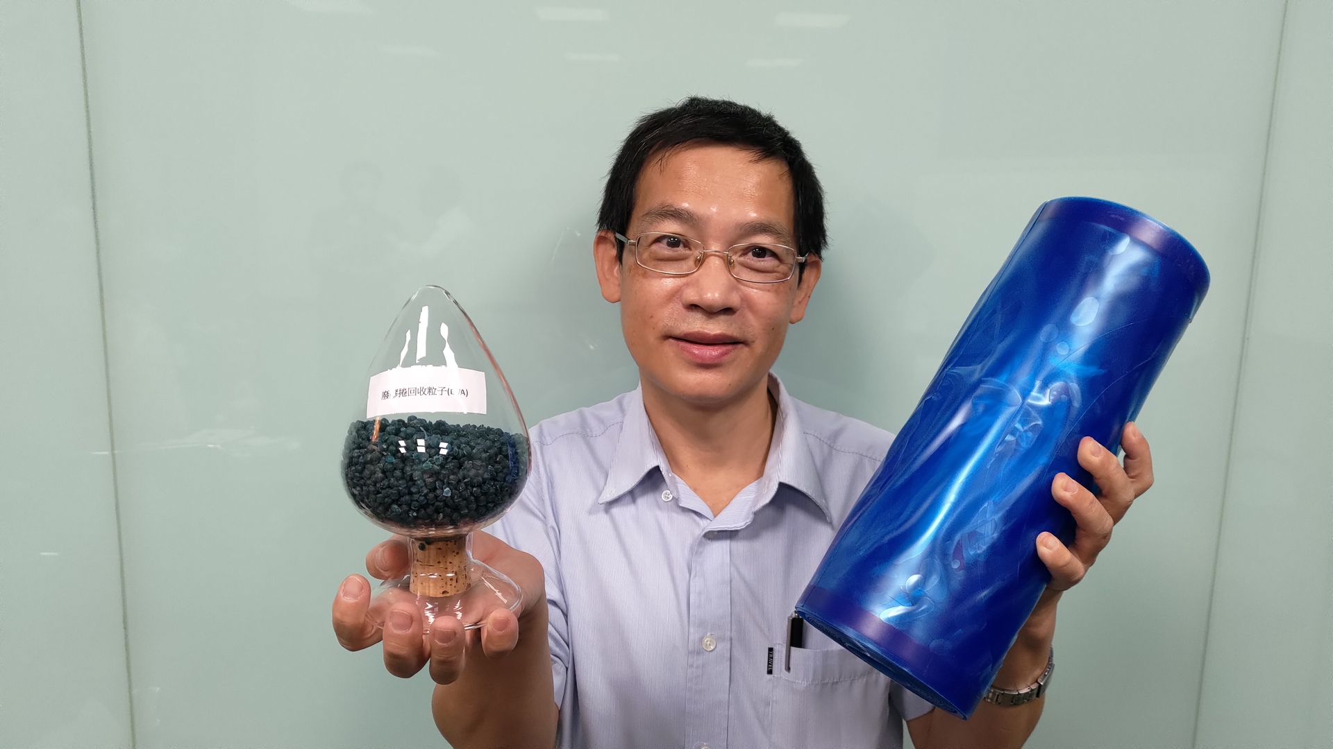 化材系教授蘇進成展示將晶圓廢棄膠帶（右，藍色捲狀）， 回收再生轉為可作為鞋大底的材料（左，深色顆粒）。