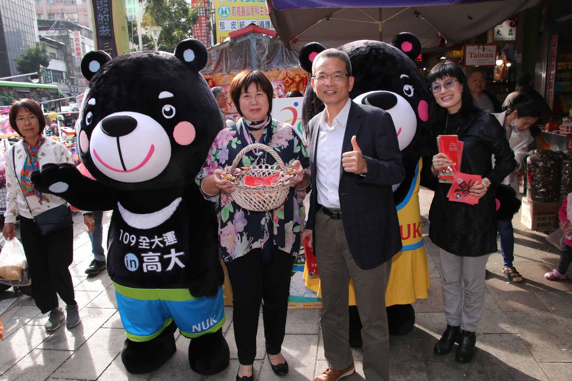 主任秘書曾榮豐、體育室主任孫美蓮與全大運吉祥物「熊高高」、「熊啦啦」陪同發送紅包袋及春聯圖片