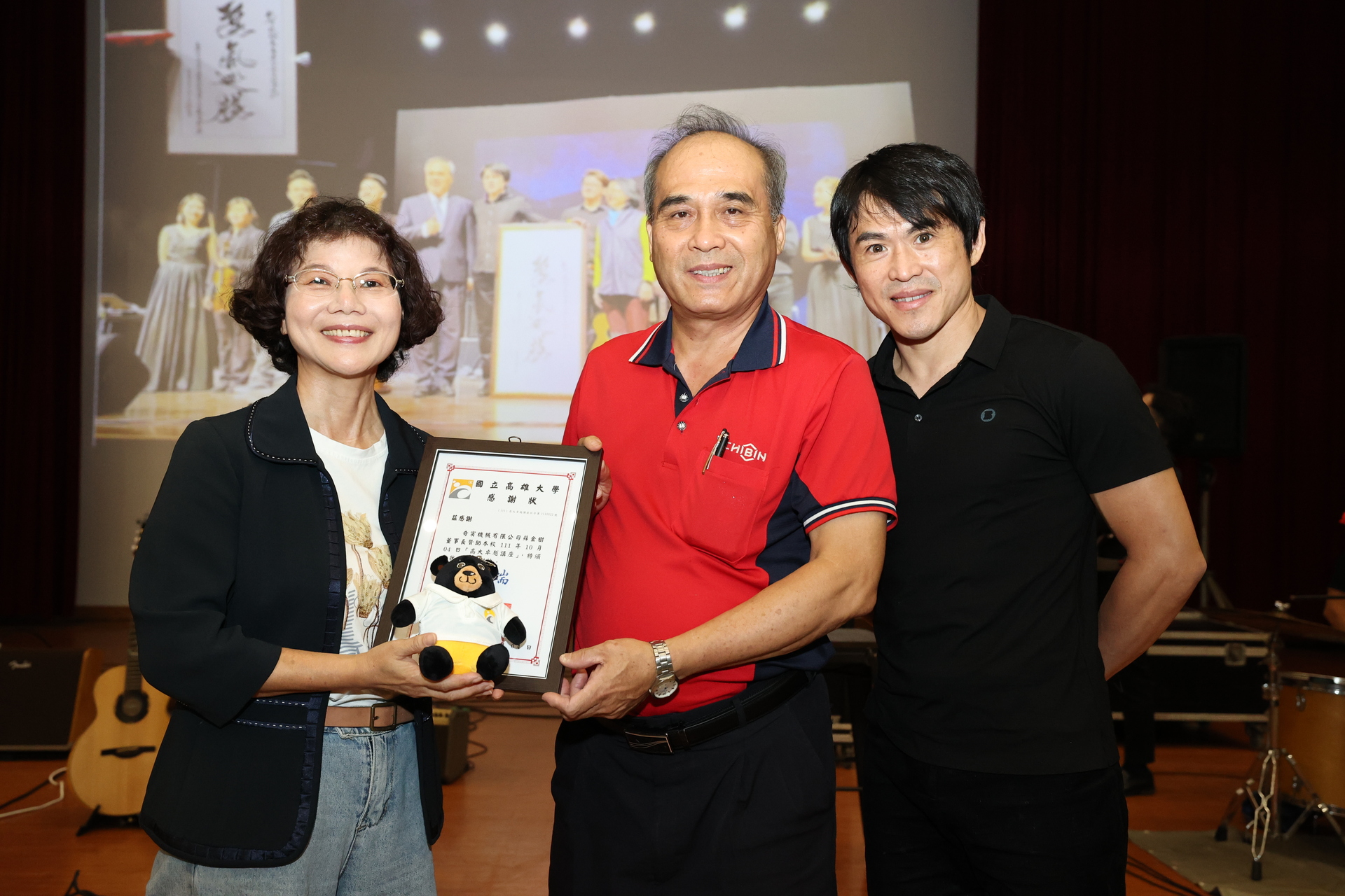 高雄大學校長陳月端（左）代表校方頒贈感謝狀予 贊助經費的EMBA99級校友蘇金樹（中），以及演出樂團、玫瑰墓團長蘇世揚。