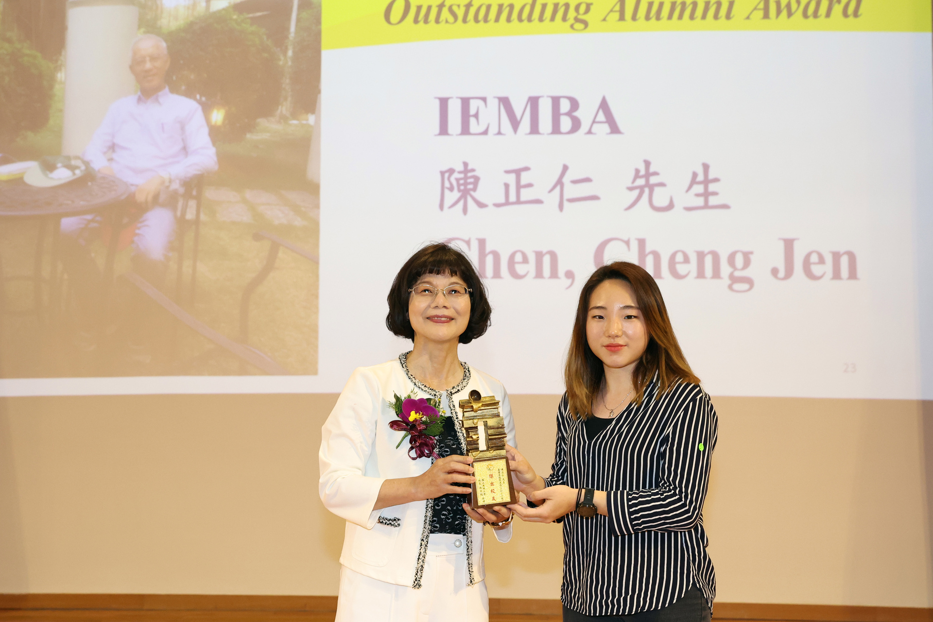 高雄大學校長陳月端（左）頒贈傑出校友獎座予IEMBA碩士陳正仁，由女兒代領。
